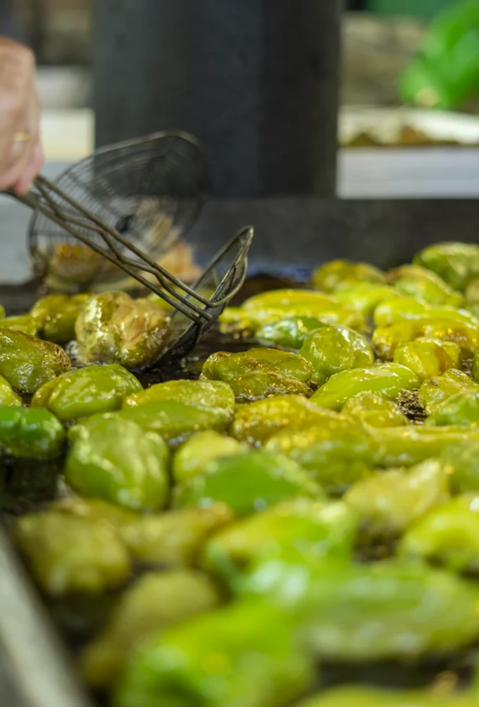 Primeiro plano de pementos da Arnoia fritindo en aceite quente cunha espumadeira