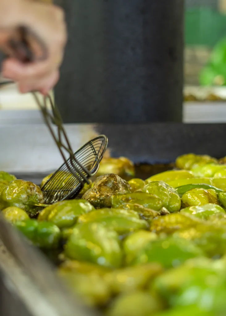 Primeiro plano de pementos de Arnoia fritindo en aceite quente cunha espumadeira