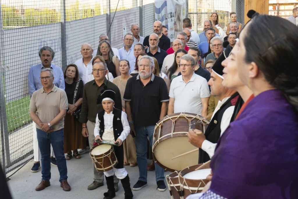 Veciños escoitan atentos os gaiteiros e tamborileiros, cun neno tocando o tambor en primeiro plano