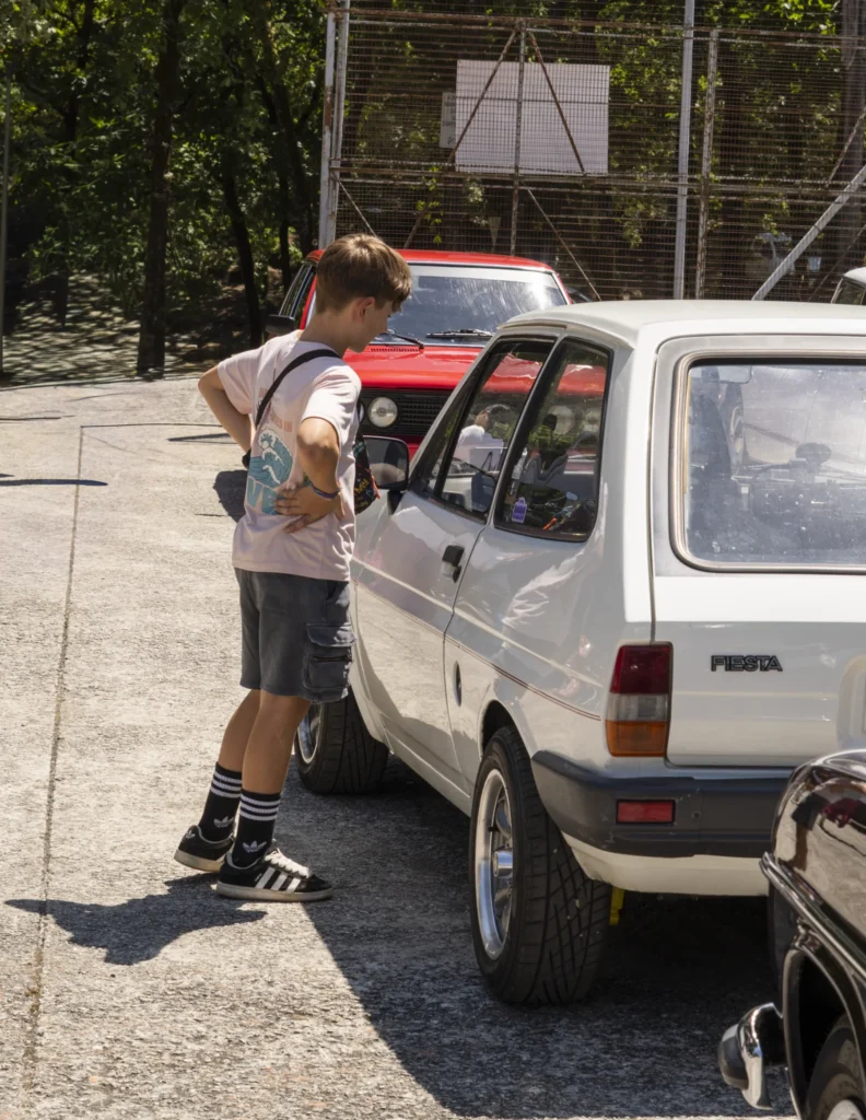 Rapaz observa un Ford Fiesta clásico branco na exposición de coches antigos da festa