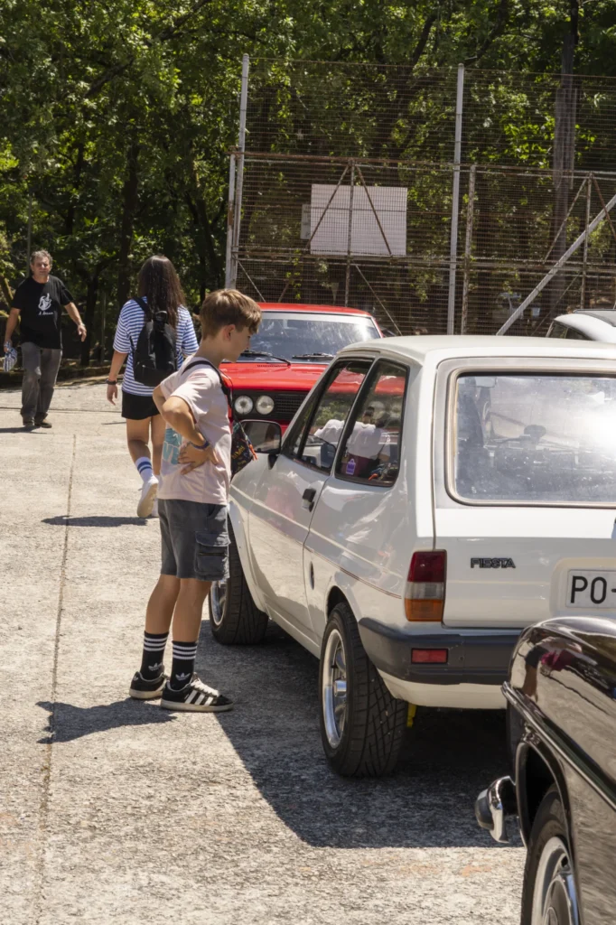 Rapaz observando un Ford Fiesta clásico na exposición de coches antigos da festa