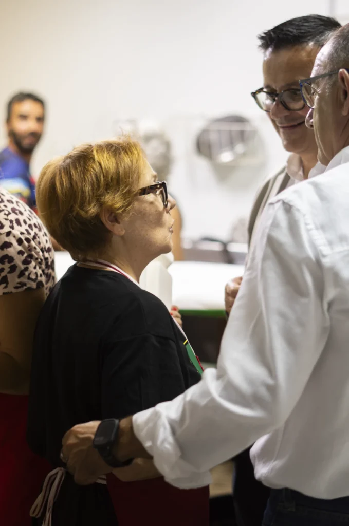 Home saúda cun abrazo a unha voluntaria con mandil na cociña do recinto da festa