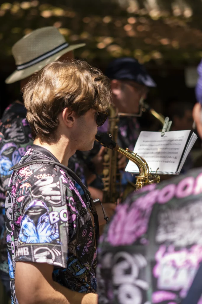 Saxofonista da charanga toca con camisa estampada mentres a banda anima o paseo da festa