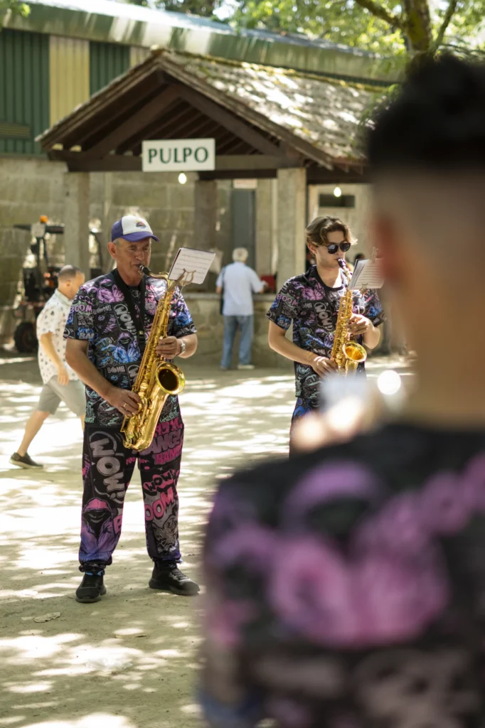 Dous saxofonistas da charanga tocan diante da caseta do pulpo no recinto da festa