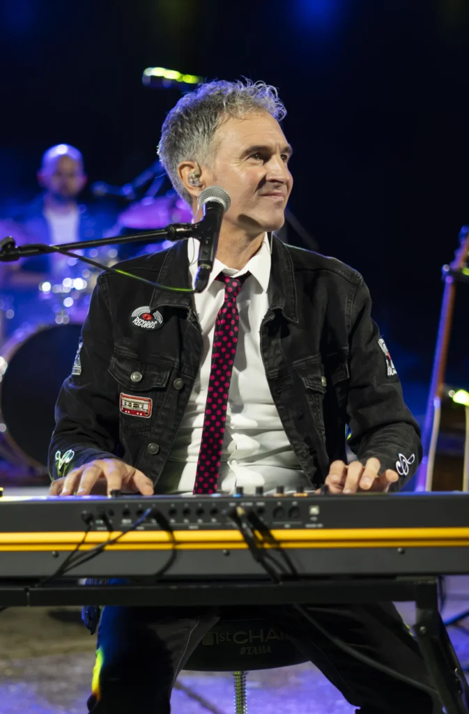 Teclista dunha banda toca no escenario nocturno con gravata de lunares e luces azuis