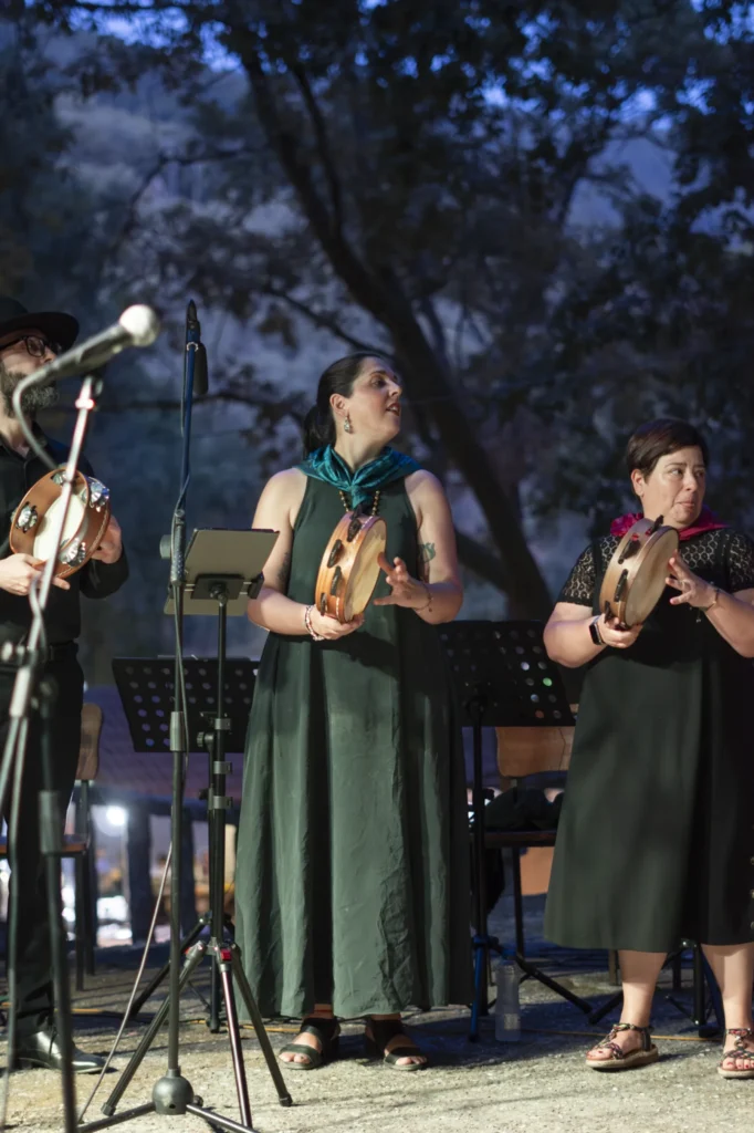 Tres cantareiras con pandeiretas actuando ao anoitecer no escenario da Festa do Pemento