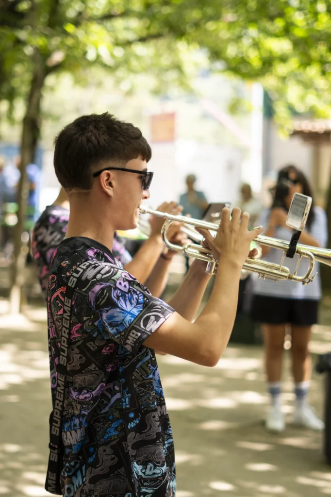 Mozo trompetista da charanga tocando á sombra das árbores do campo da festa