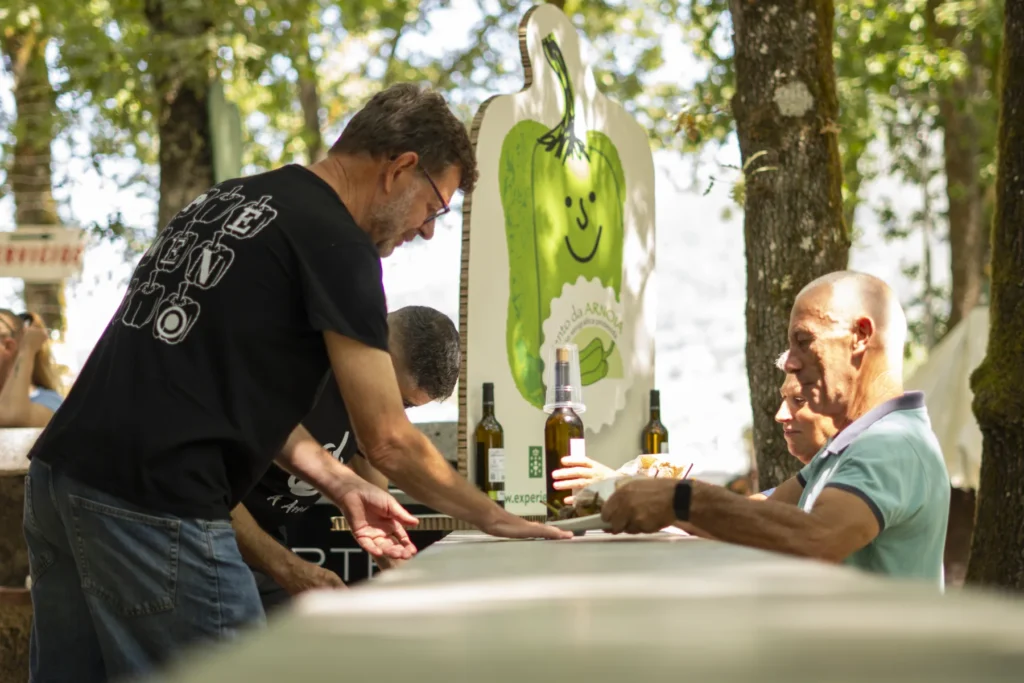 Voluntario servindo unha ración xunto ao panel do pemento sorrinte e as botellas de viño