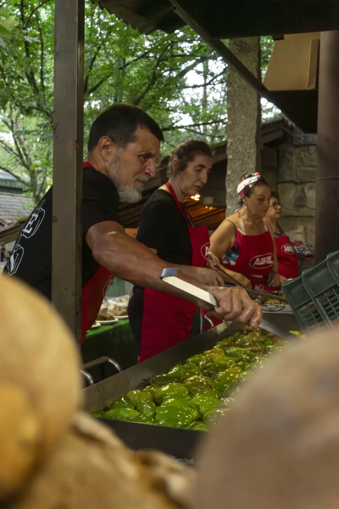 Voluntarios con mandís vermellos fritindo pementos da Arnoia nunha grande fritideira ao aire libre