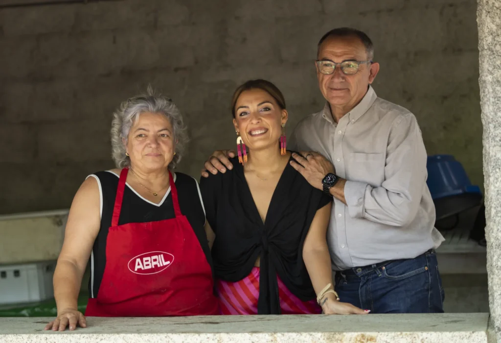 Tres voluntarios do posto de pementos posan sorrindo na ventá da cociña do recinto
